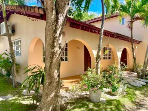 Peach arched-veranda cottage rental in Nassau surrounded by tropical garden and trees.