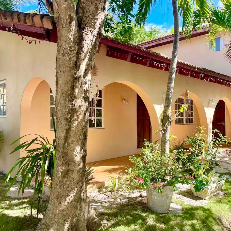 Peach arched-veranda cottage rental in Nassau surrounded by tropical garden and trees.